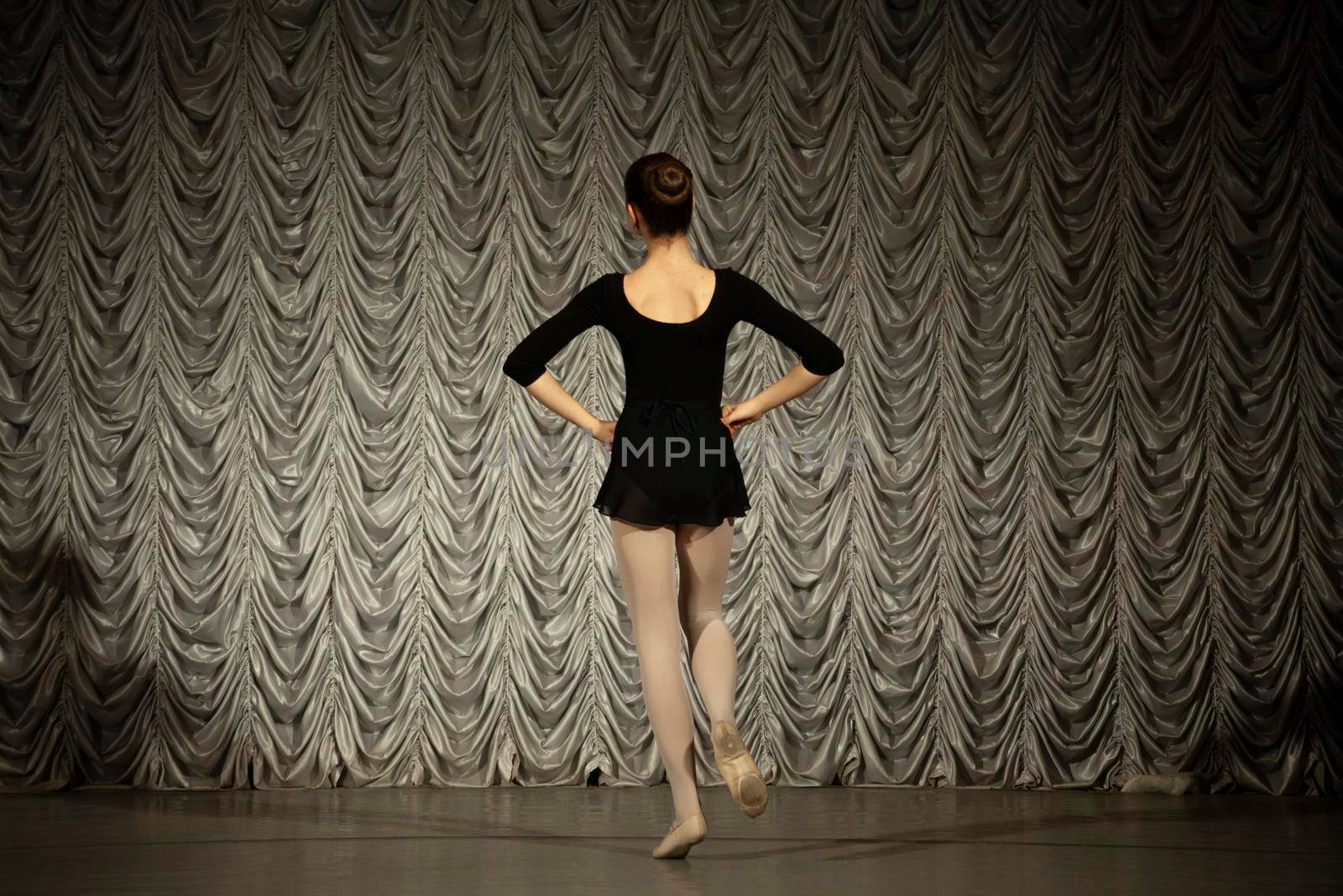 Ballerina on stage. Dance lesson. Schoolgirl performs gymnastics. Girl in black dress. Dance school.