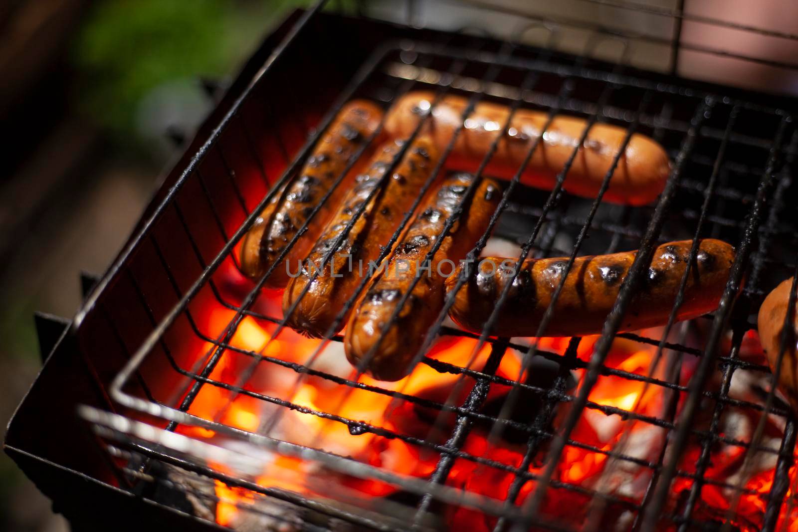 Sausages are roasted over fire. Barbecue in evening on street. Cooking meat on open flame. Warming up food for dinner. Juicy sausages covered with crust of baked meat.