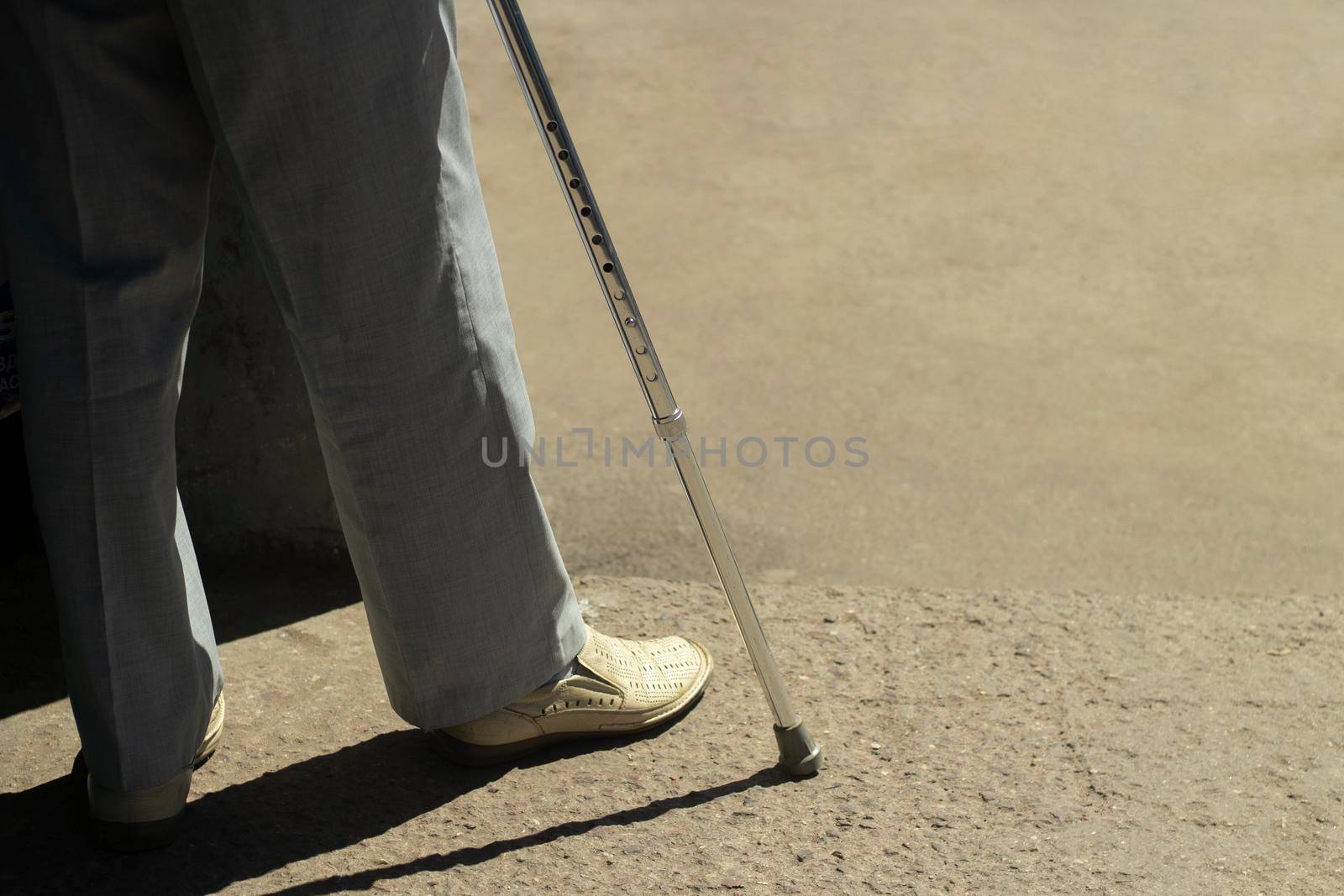 Walking stick. A man with a leg injury. Disabled with a device for support when walking An old man in white shoes.