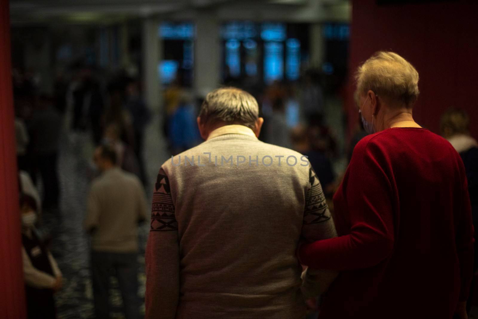 People are walking inside building. Lot of people leave room. Old people after concert. Seniors walk up stairs.