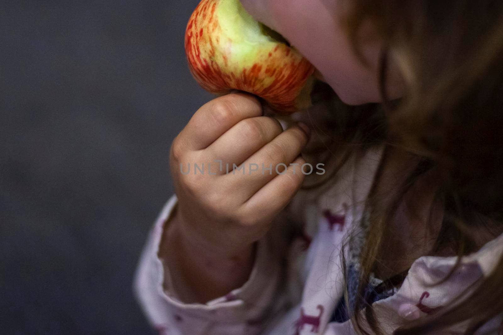 Child bites apple. Girl eats fruit. Healthy food in morning. Preschooler's breakfast. Fresh apple in hands of girl. by OlegKopyov