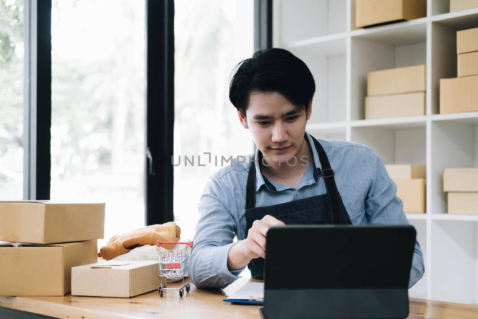 Asian business men use laptop computer checking customer order online shipping boxes at home. Starting Small business entrepreneur SME freelance. Online business, Work at home concept. by wichayada