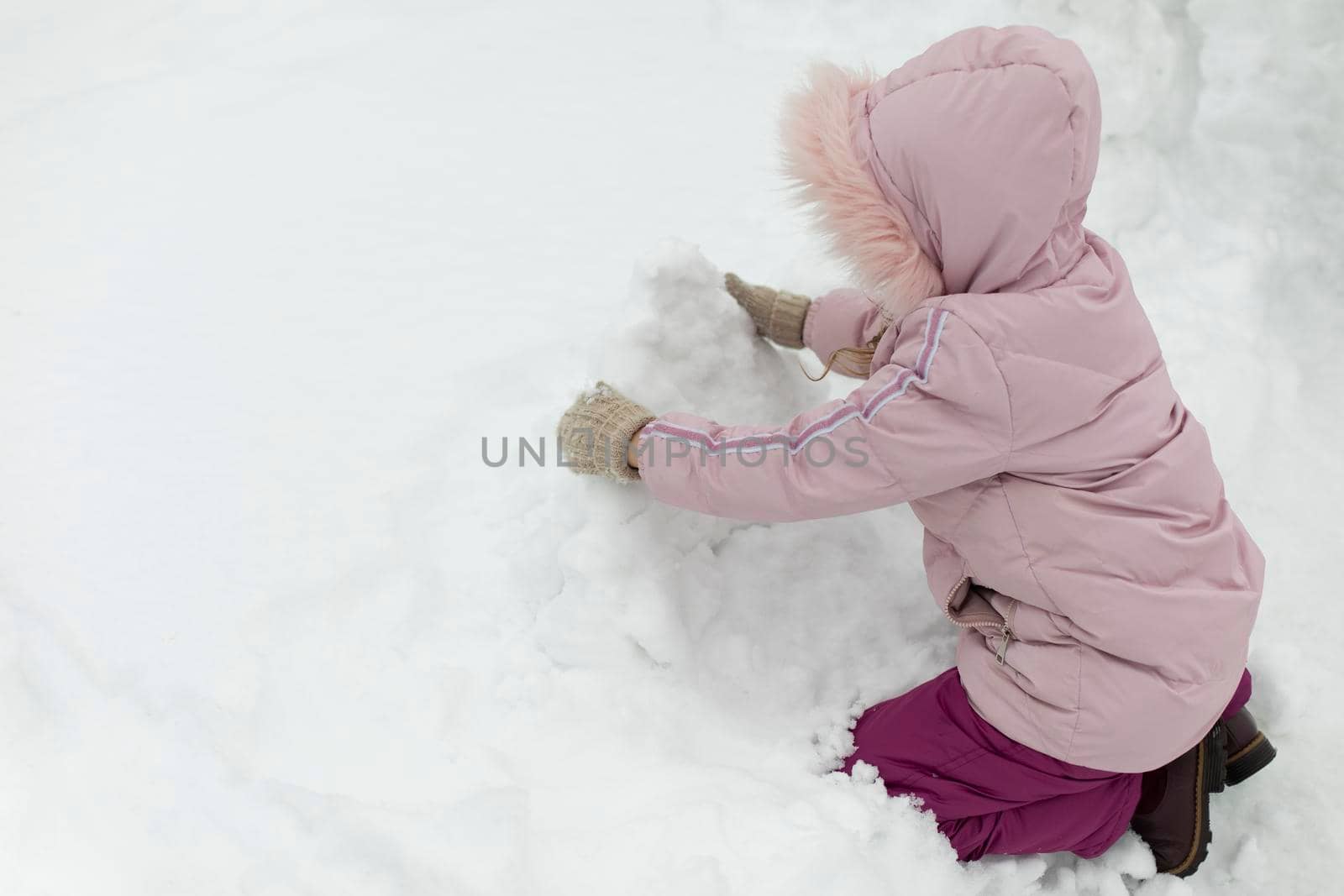 Child sculpts snowman. Girl plays in snow. Baby in winter on street. by OlegKopyov