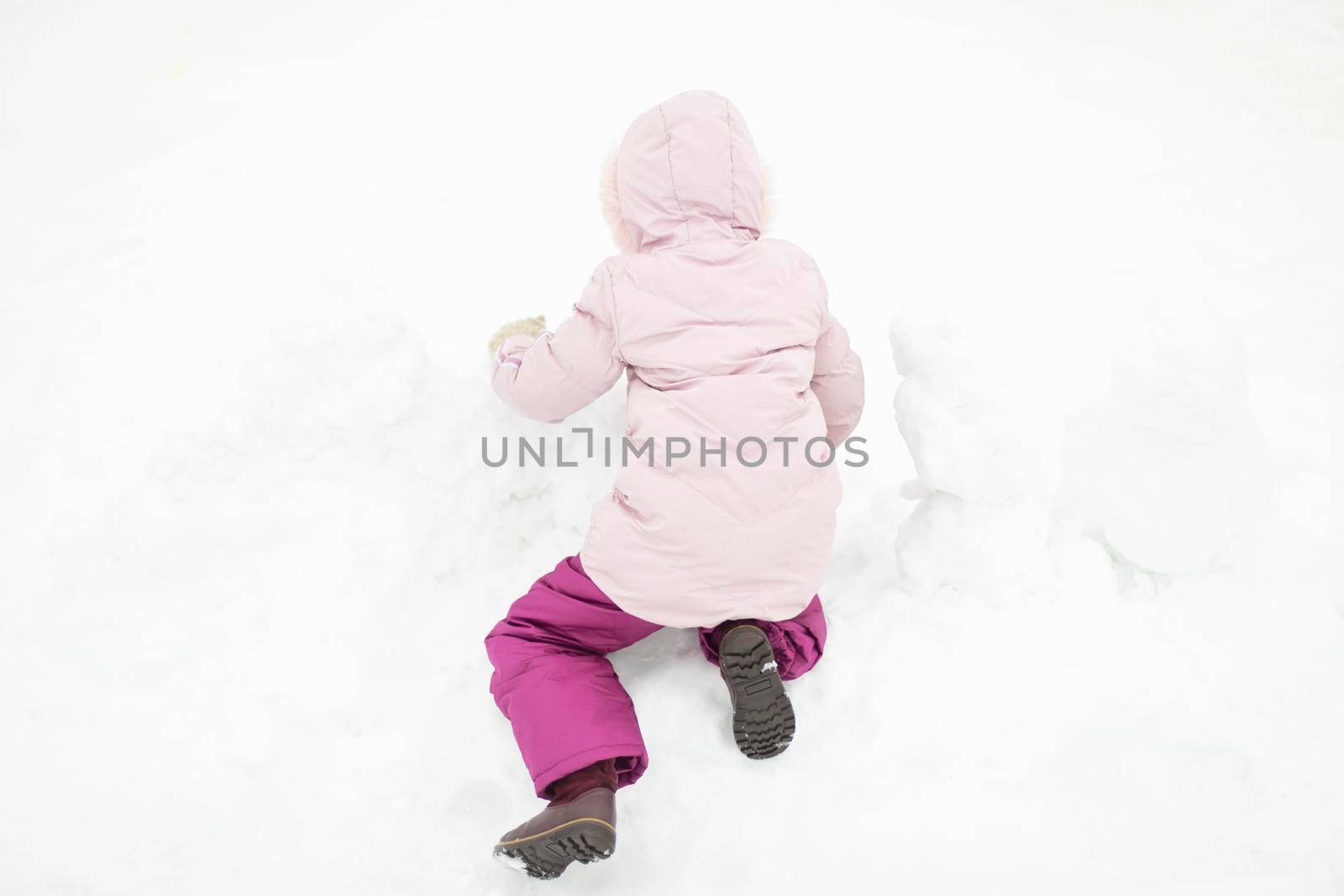 Child plays in snow. Girl in winter. Warm clothes on child. Winter walk in yard.