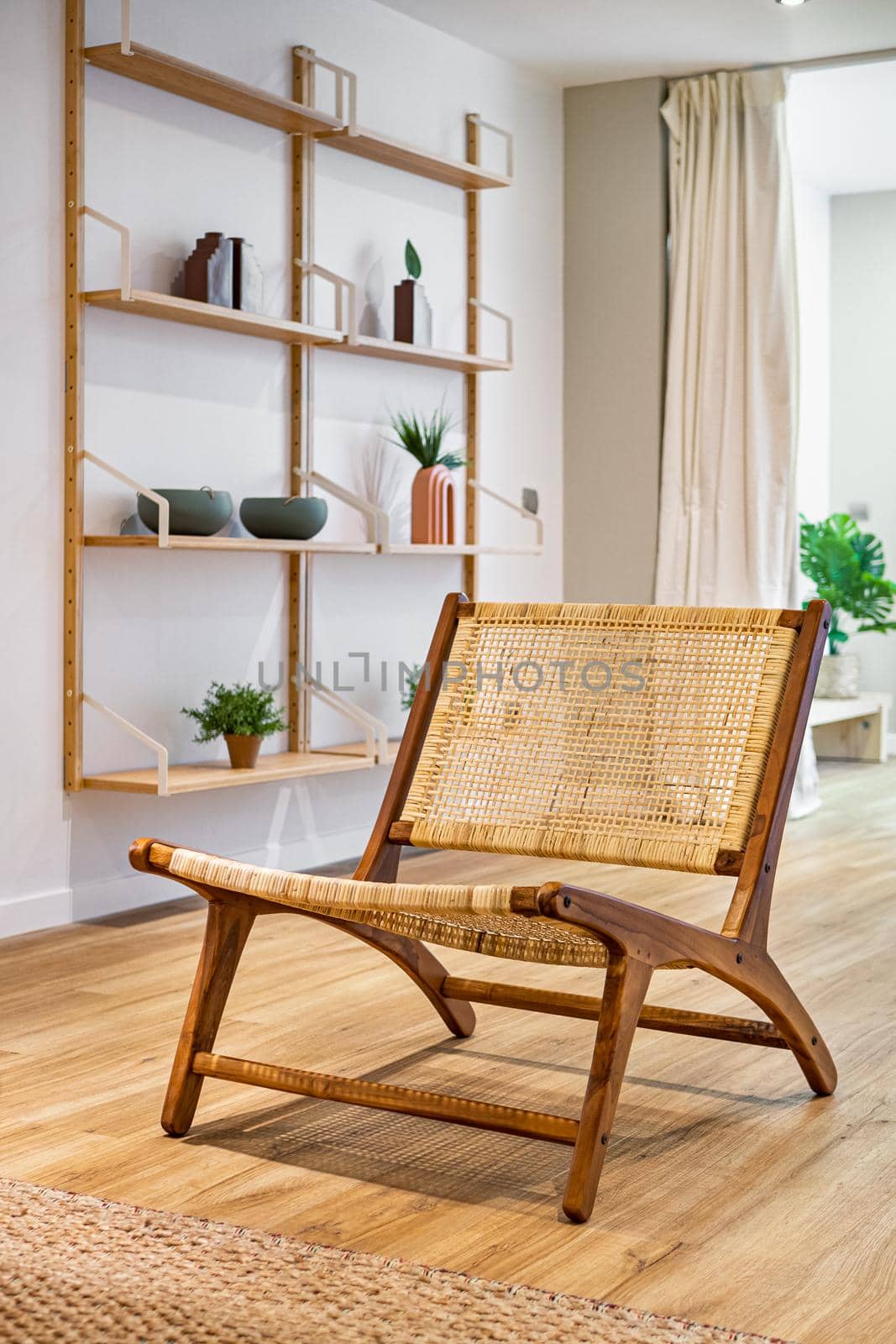 Modern wicker chair standing in living room with gray wall and shelves with decorations and plants. Interior wooden furniture.