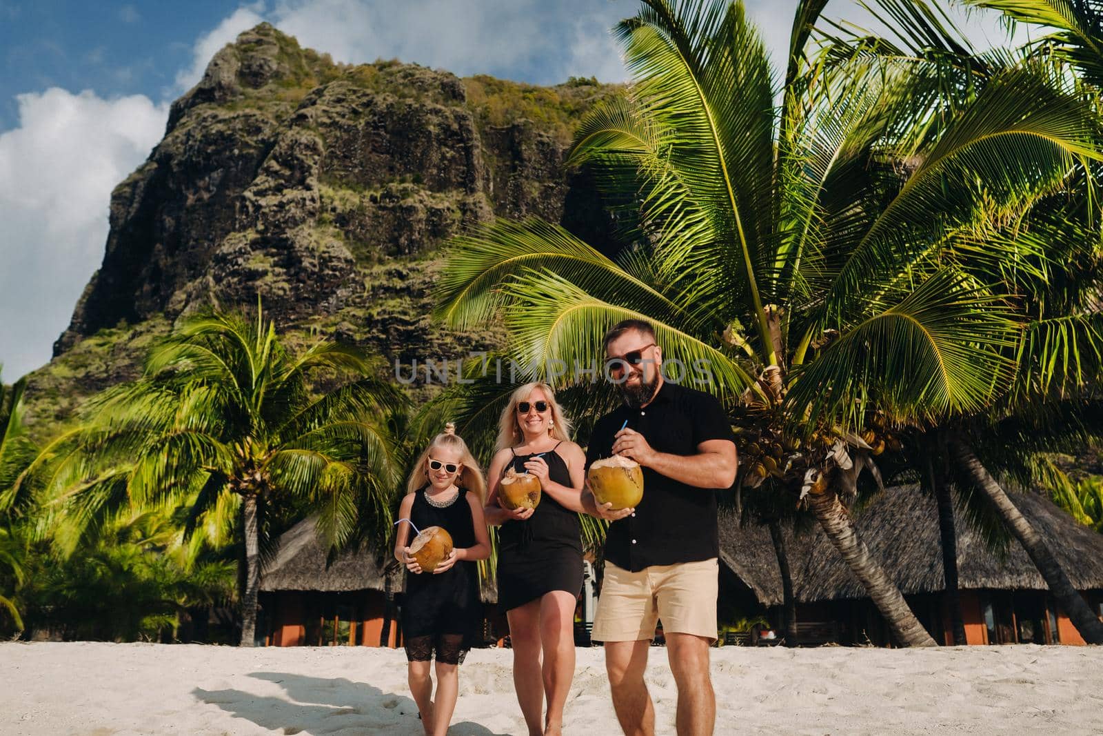 a stylish family in black clothes with coconuts in their hands on the beach of the island of Mauritius.Beautiful family on the island of Mauritius in the Indian ocean.