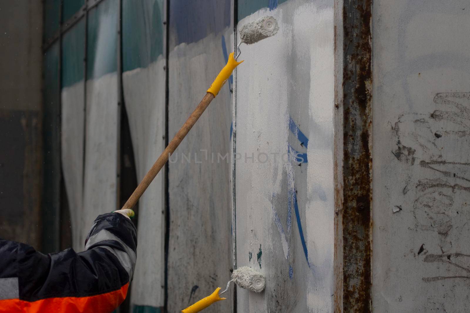 The painter paints with white paint. Paints graffiti with paint. Painting the wall. A worker paints over a vandalist inscription.