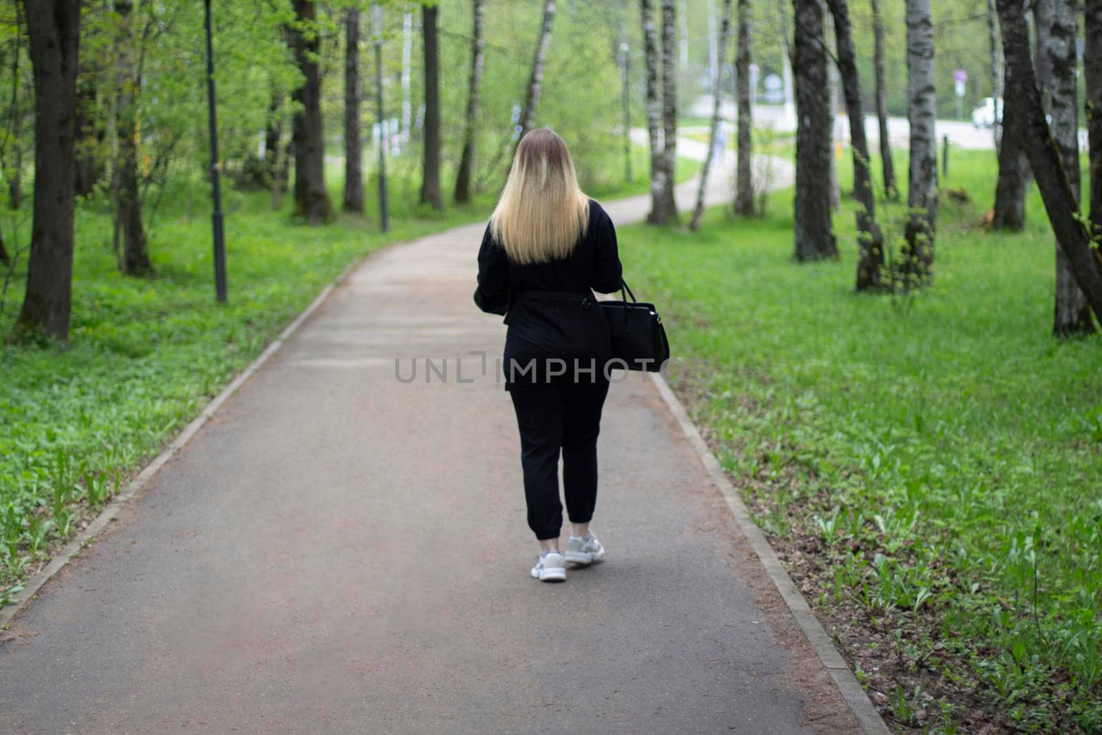 The girl is walking in the park. A woman from the back in the street. A woman walks down the street alone.