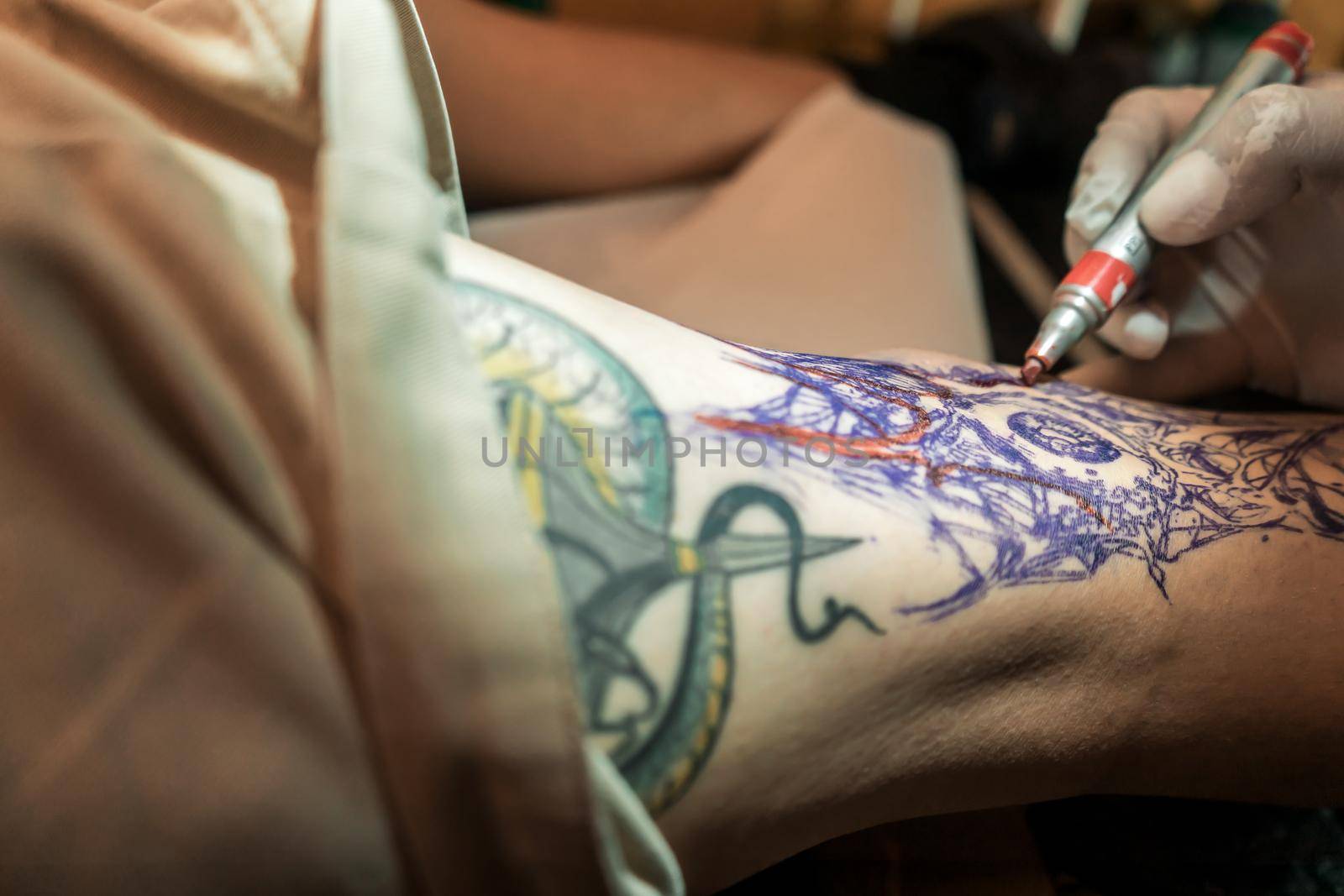 Closeup of the hand of a Latino tattoo artist marking the sketch of a tattoo on a man's leg with a red marker.