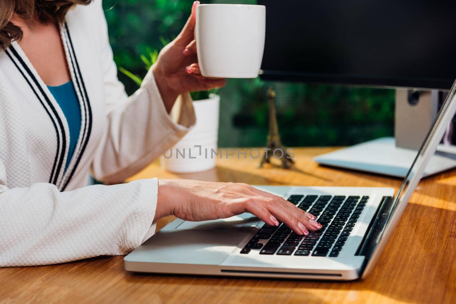 Beautiful business woman lifestyle working using laptop computer and holding coffee cup on hand while enjoying in modern desk office near window, work from home concept