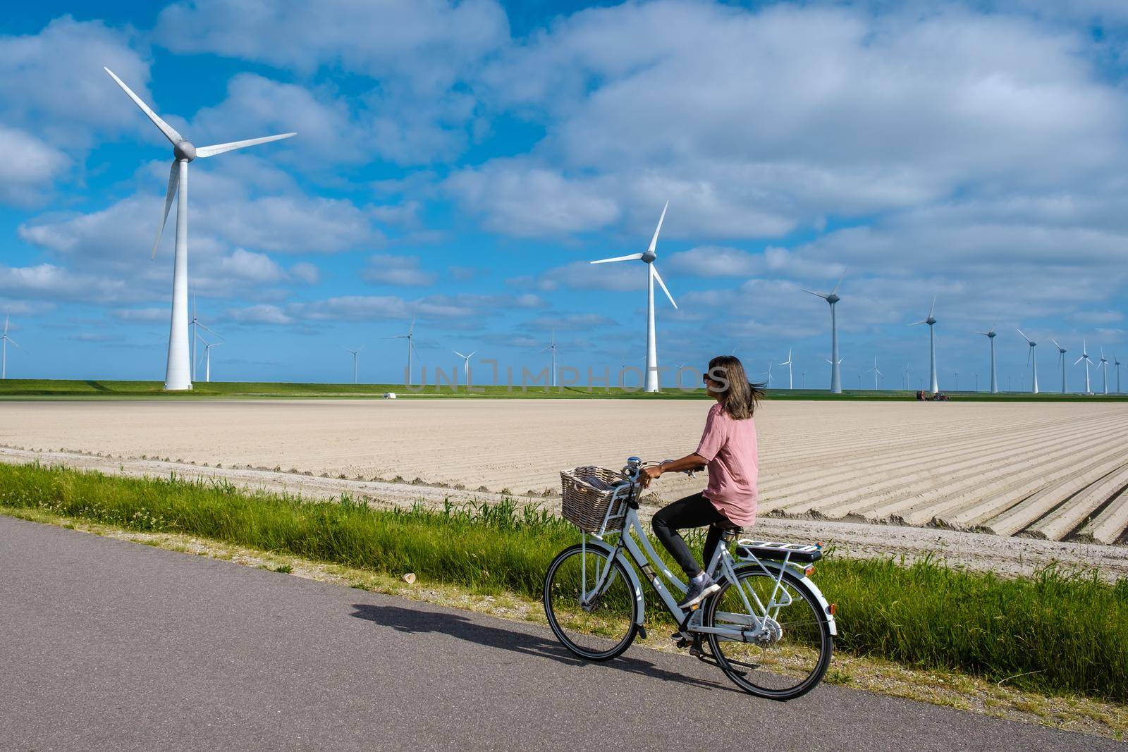 young woman electric green bike bicycle by windmill farm , windmills isolated on a beautiful bright day Netherlands Flevoland Noordoostpolder by fokkebok