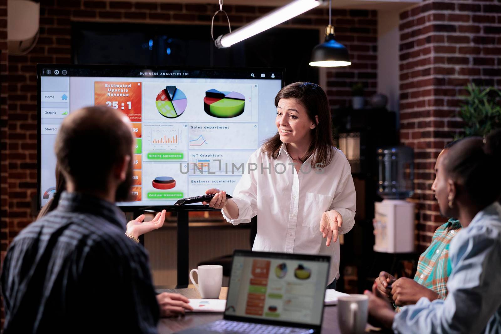 Smiling caucasian woman in startup office doing business presentation on big tv screen with charts by DCStudio