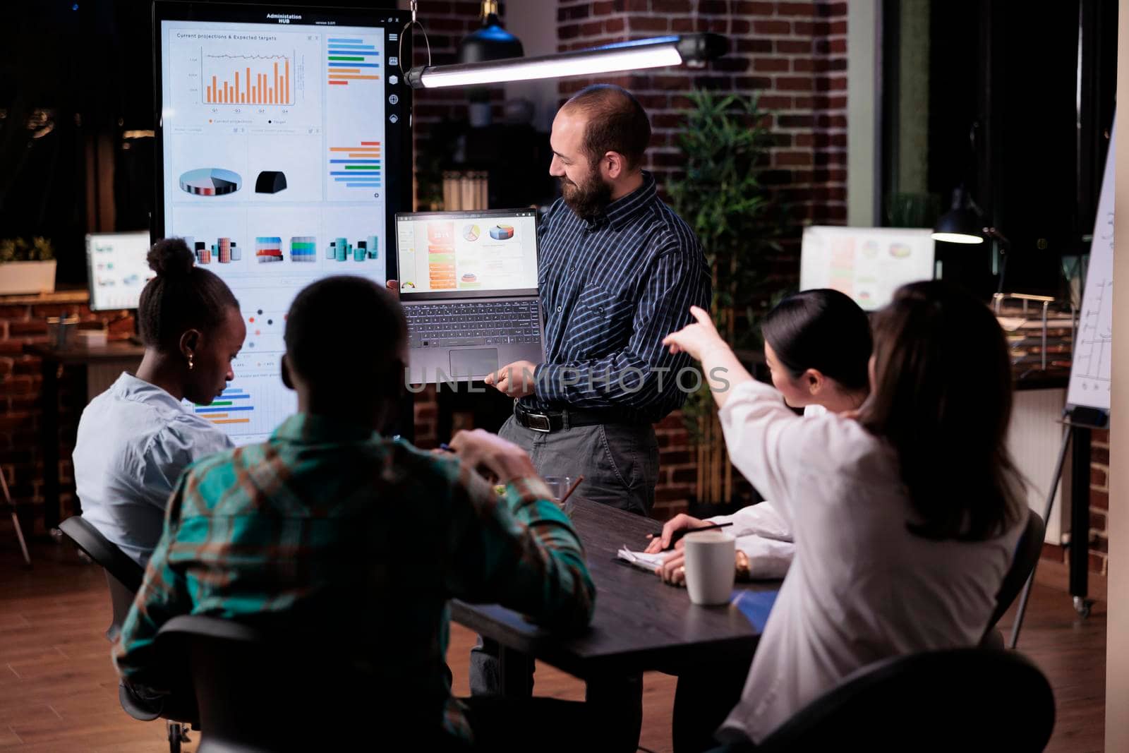 Office worker holding laptop with business presentation looking at screen while coworker is pointing at charts by DCStudio