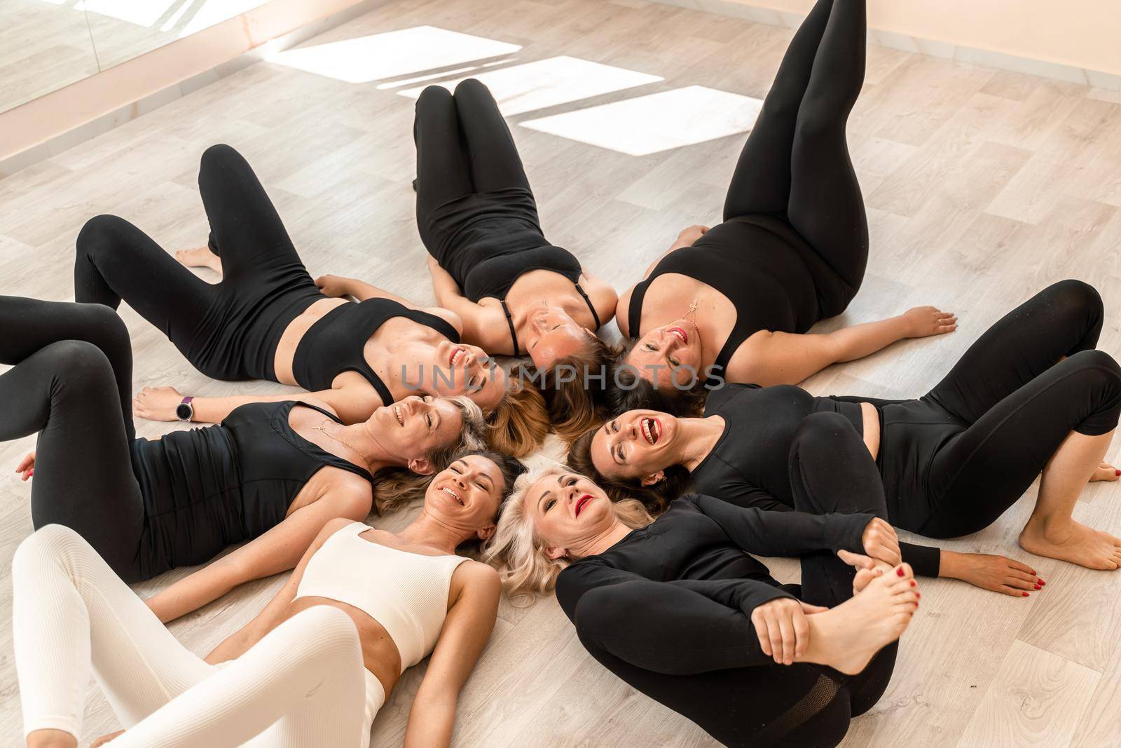 Seven happy women lie on their backs on the floor with their hea by Matiunina