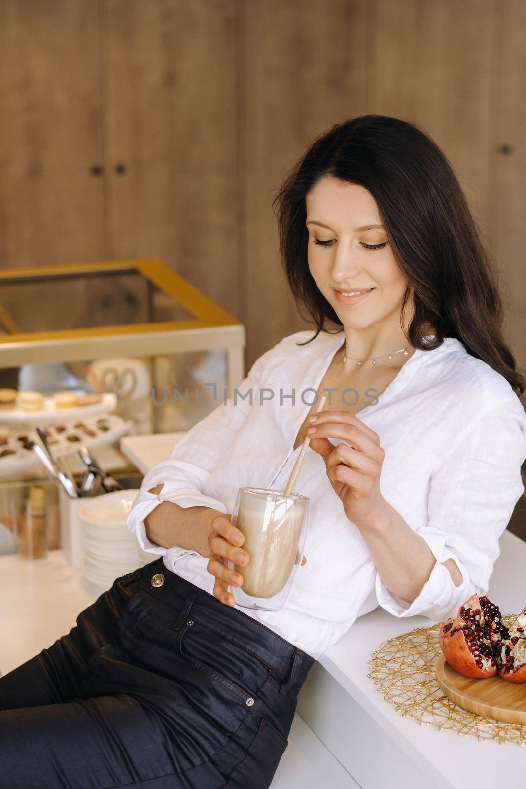 A happy healthy woman is holding a fruit cocktail in her hands, standing at home in the kitchen.Healthy eating.