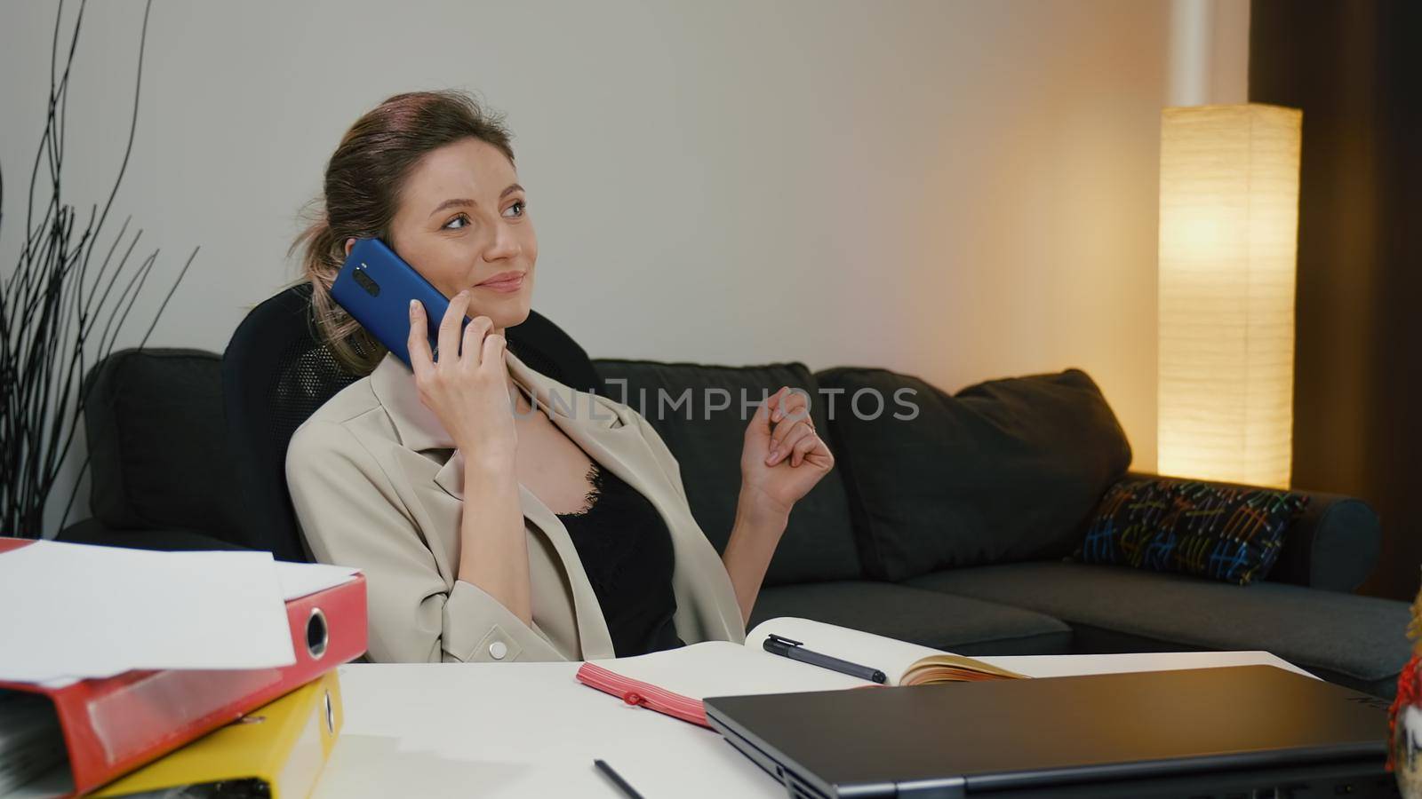 Business woman portrait talking enthusiastically on the phone at home office table after finishing work. by RecCameraStock