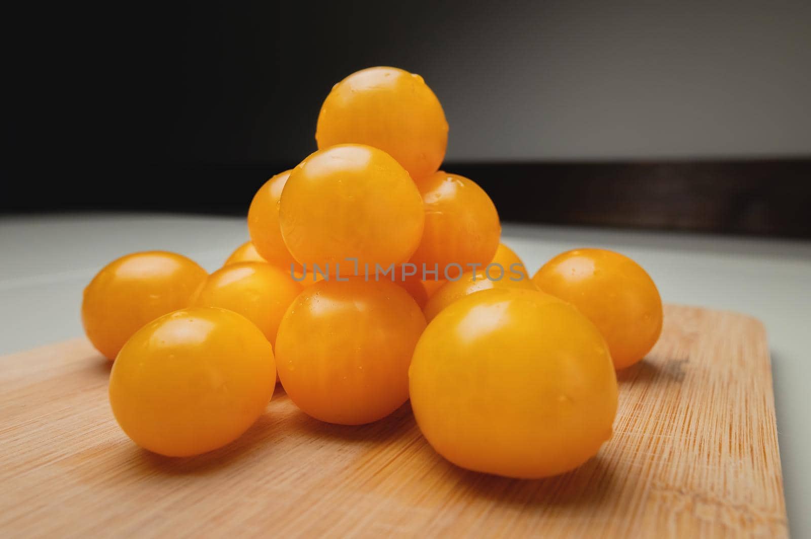 Close-up shot of yellow cherry tomatoes on a wooden cutting board in the kitchen on a white table by yanik88