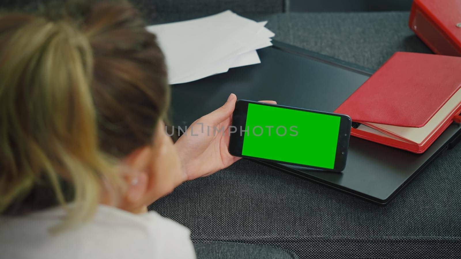 Woman sitting on a sofa with smart phone in horizontal mode with mock up green screen chroma key display. Hand of man holding mobile smart phone with chroma key, new technology concept.