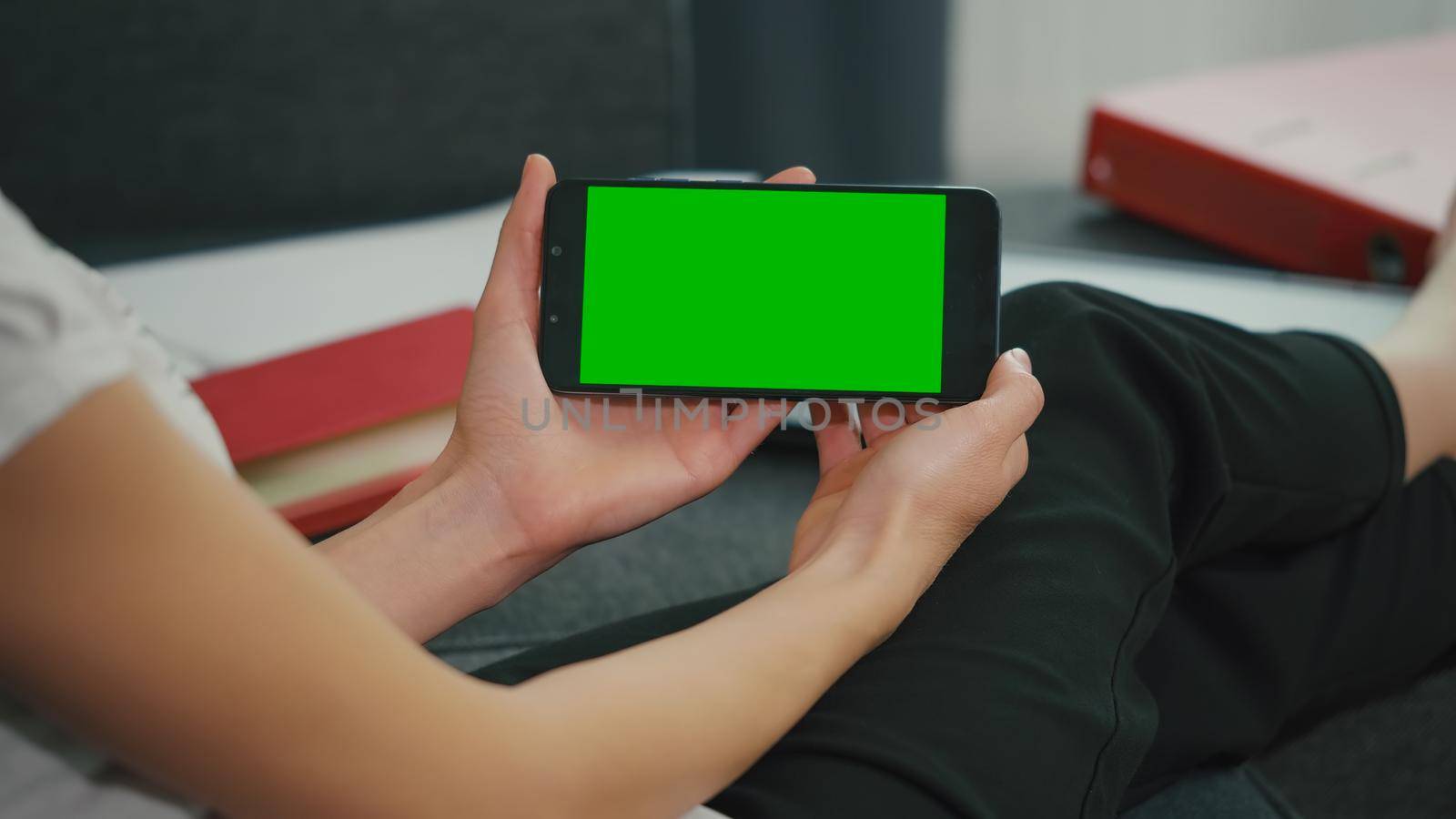 Woman sitting on sofa while looking at movies using phone with green screen display. by RecCameraStock