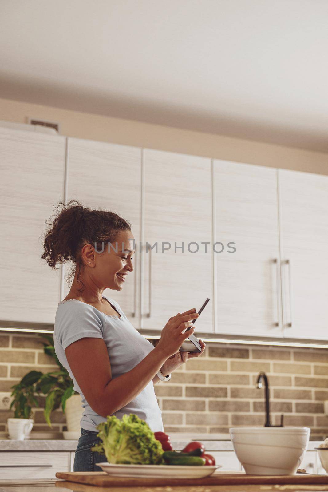 A young woman in the kitchen holds a tablet in her hands communicating in a chat by Yaroslav_astakhov