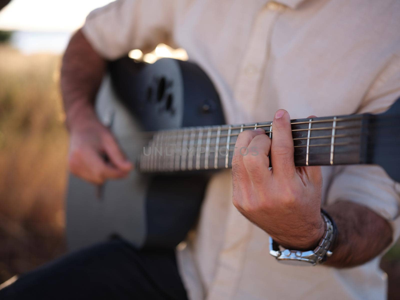 focusing on hands while playing the guitar, male person with shirt and watch, blurred background
