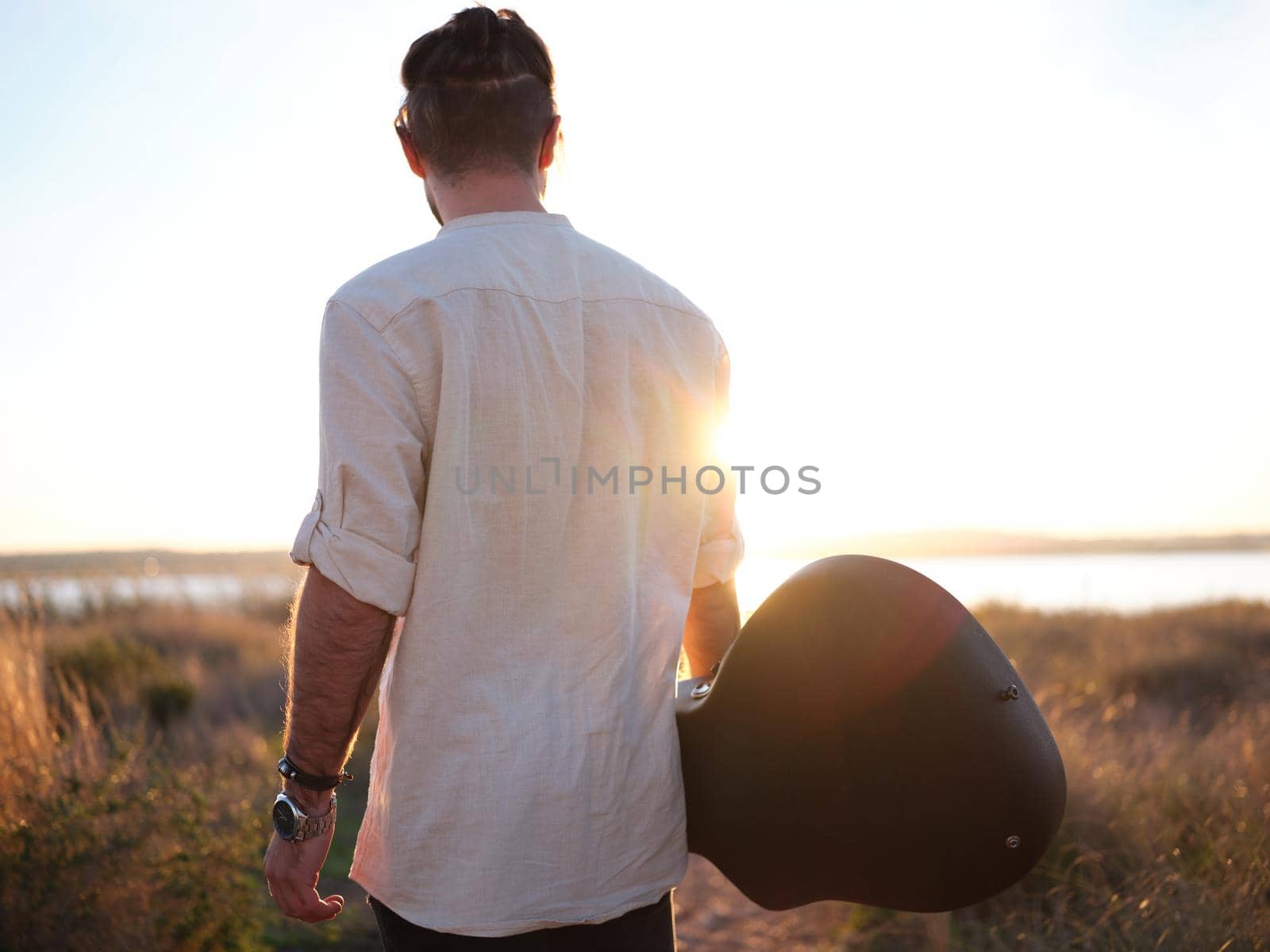 standing guitarist enjoying the sunset over a lake, looking at the horizon, horizontal waist up view