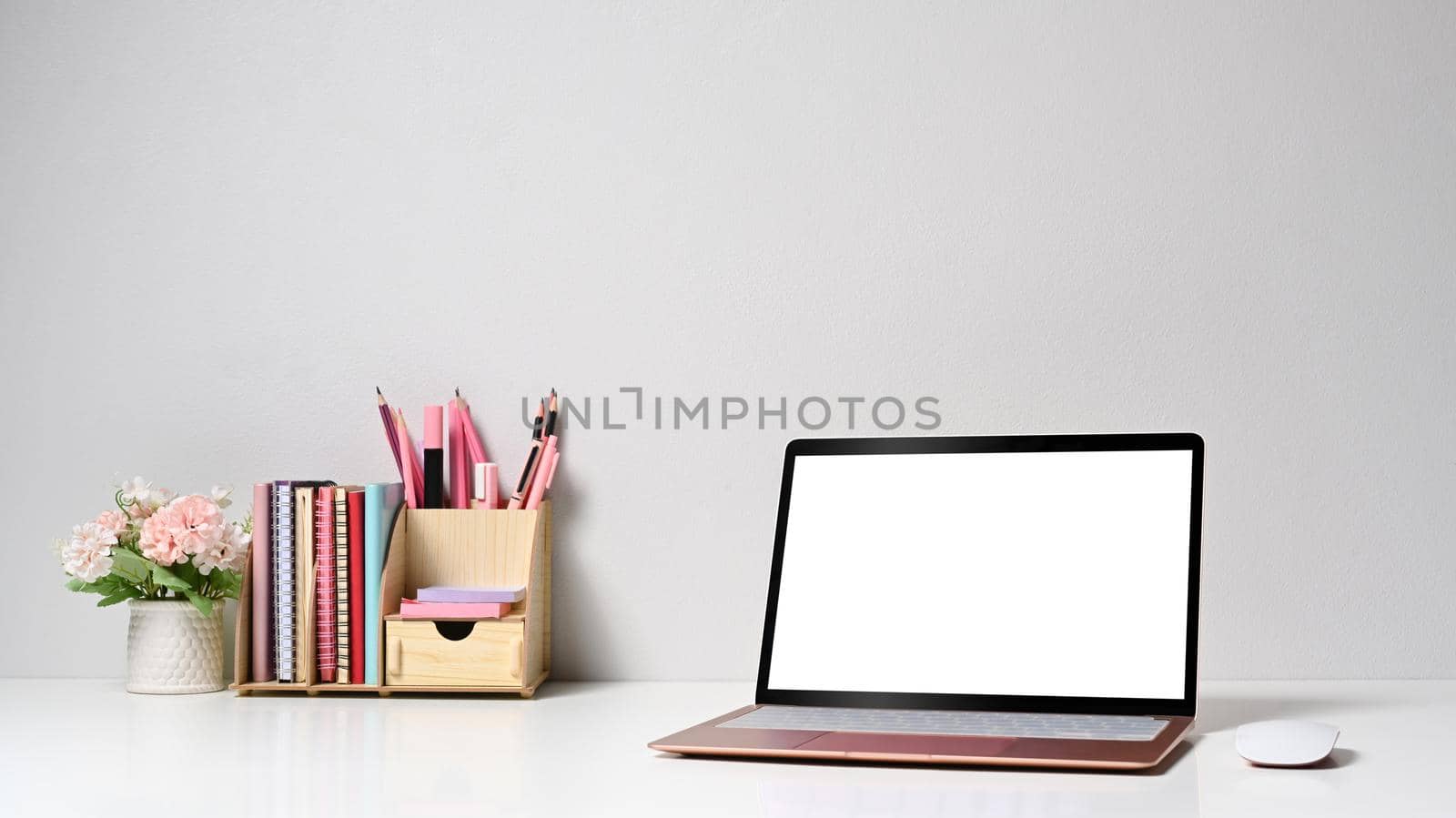 Front view computer laptop, flower pot and stationery on white table.