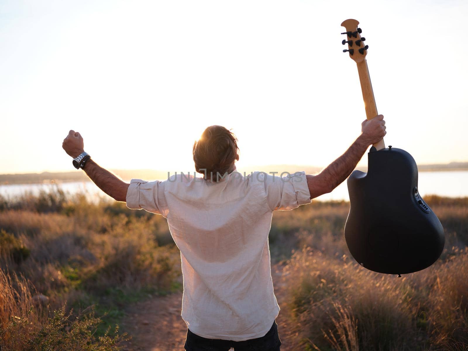 man screaming to the sky his freedom while holding a guitar in his hand up high, horizontal sunset view in the background