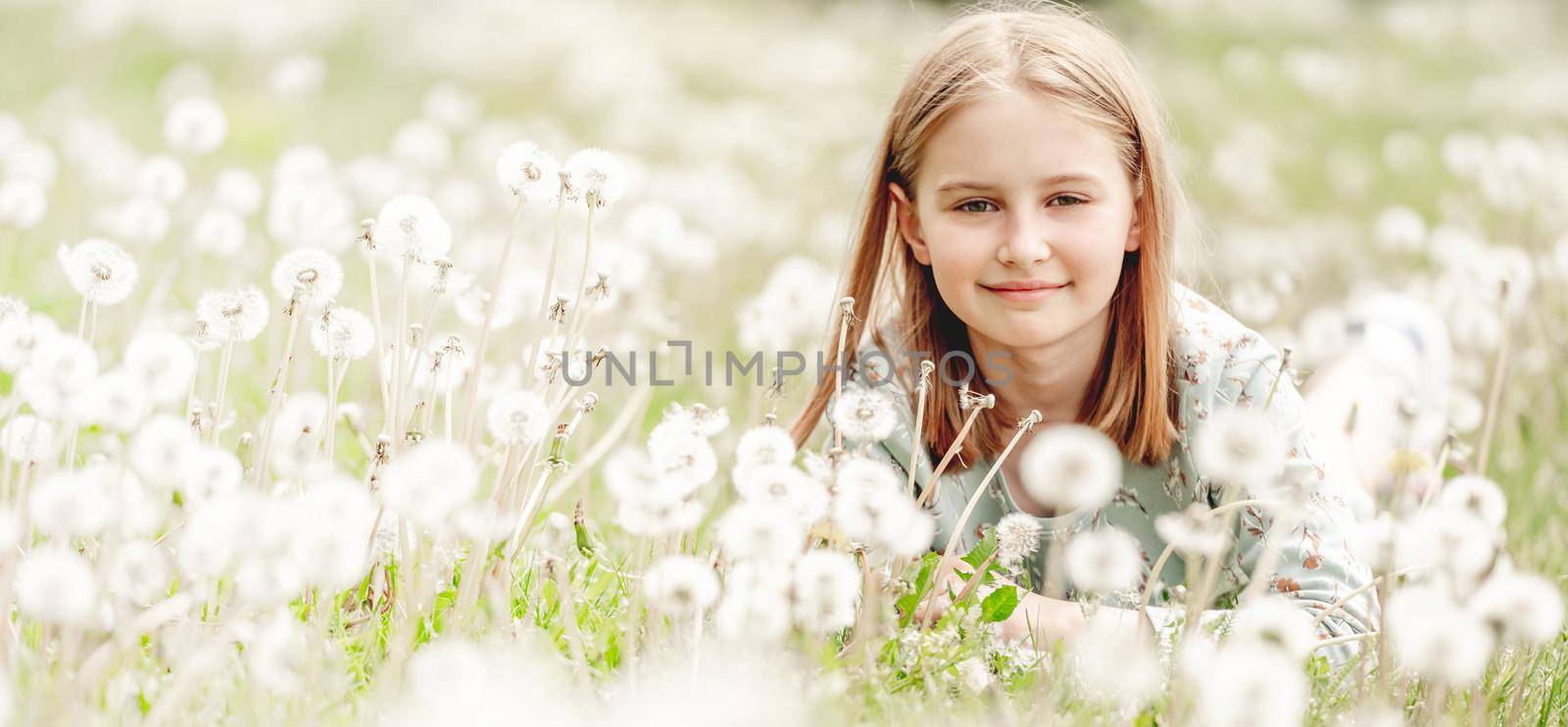 Little girl sitting in blowballs flowers field and smiling. Cute child kid with dandelions at nature