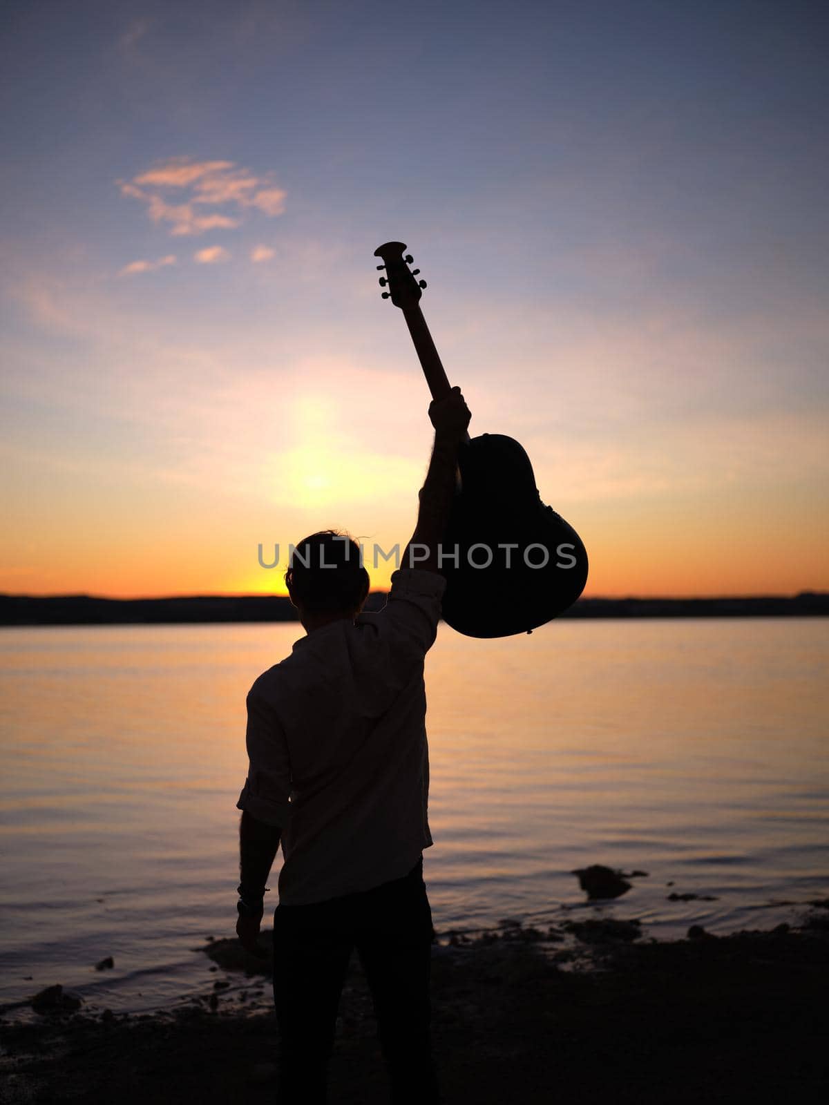 male guitarist with his guitar in the air at dusk in front of a lake by WesternExoticStockers