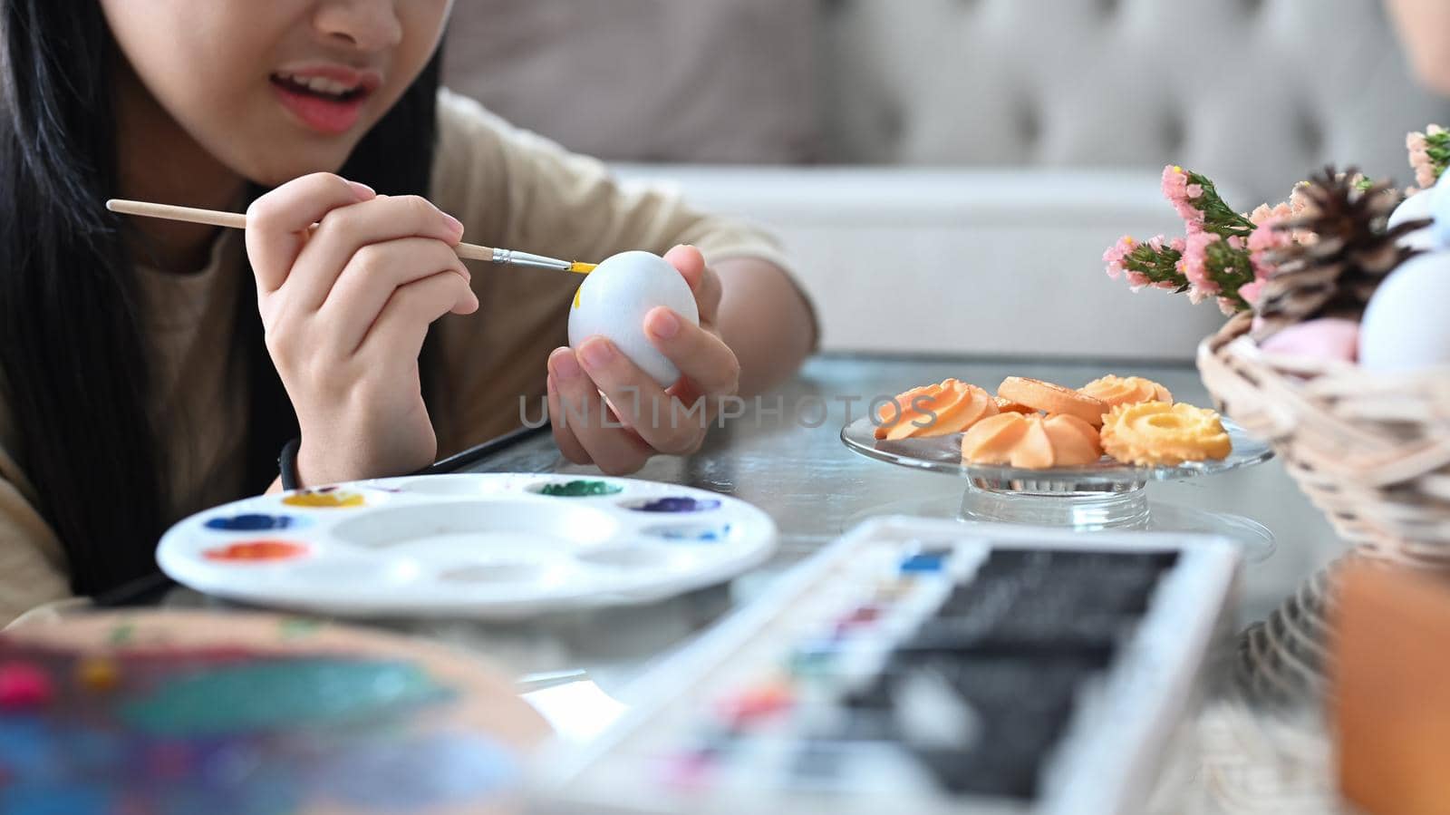 Happy little girl painting Easter eggs. Easter, holidays and people concept