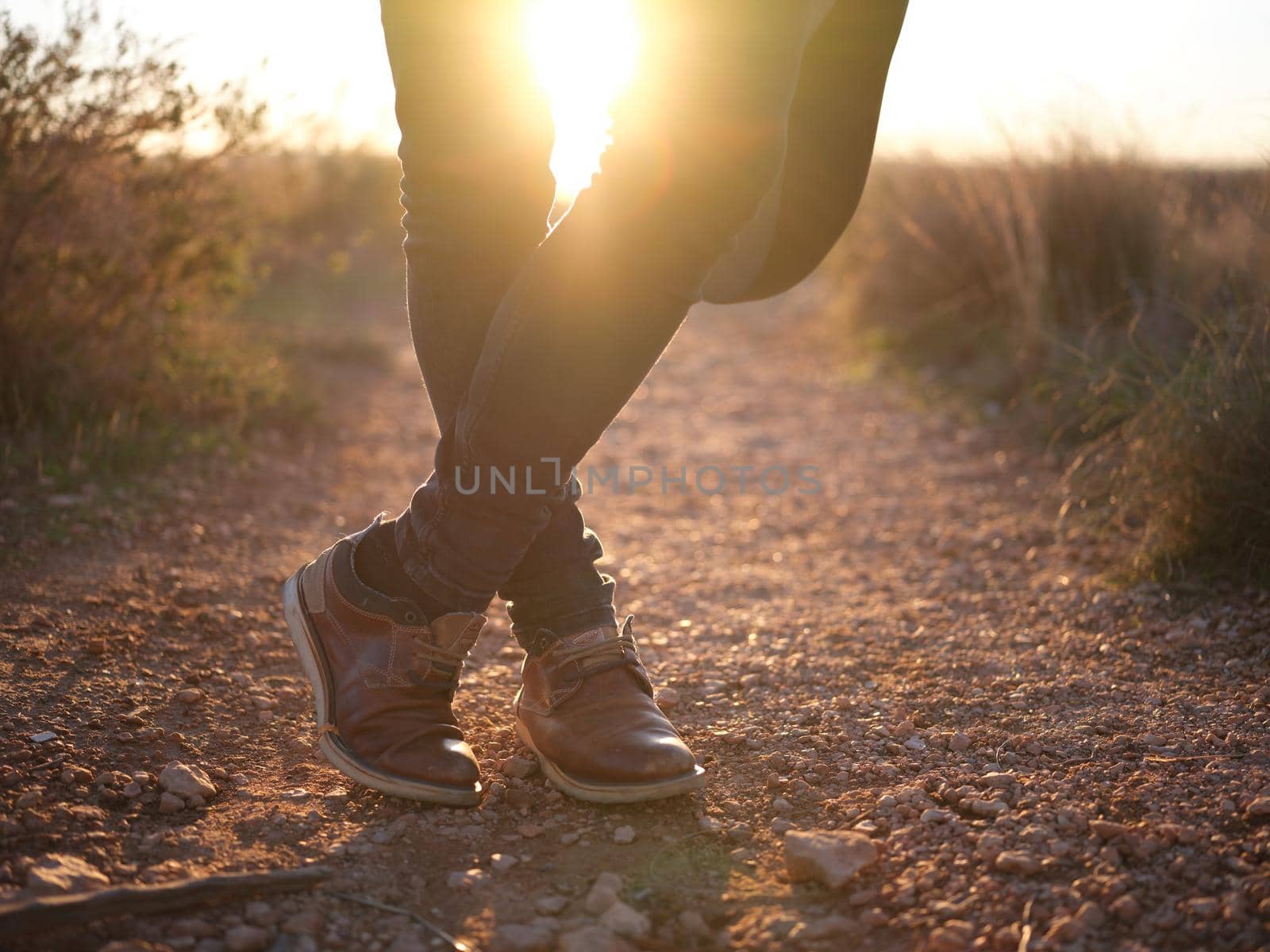 person's legs crossed with the sun passing through them at sunset in the nature, horizontal background