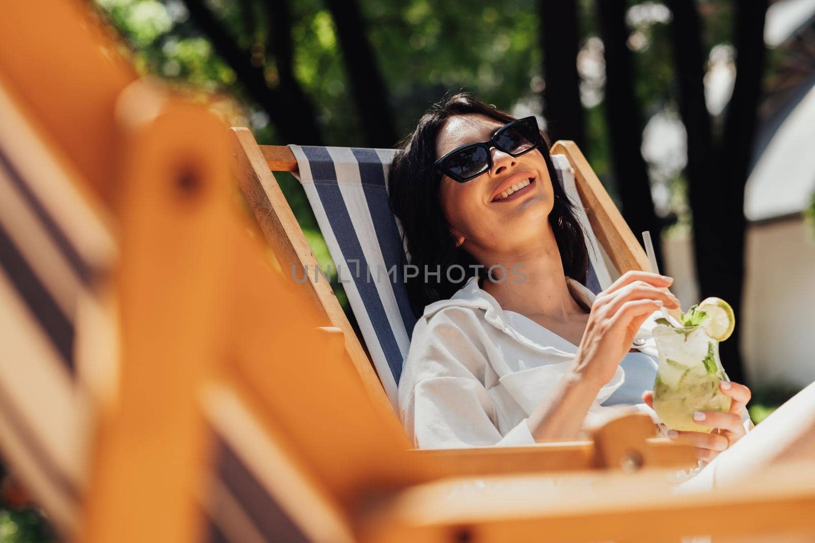 Cheerful Young Brunette Woman Relaxing and Drinking Cocktail While Sitting on the Terrace Outdoors, Girl Enjoying Summer Sunny Day