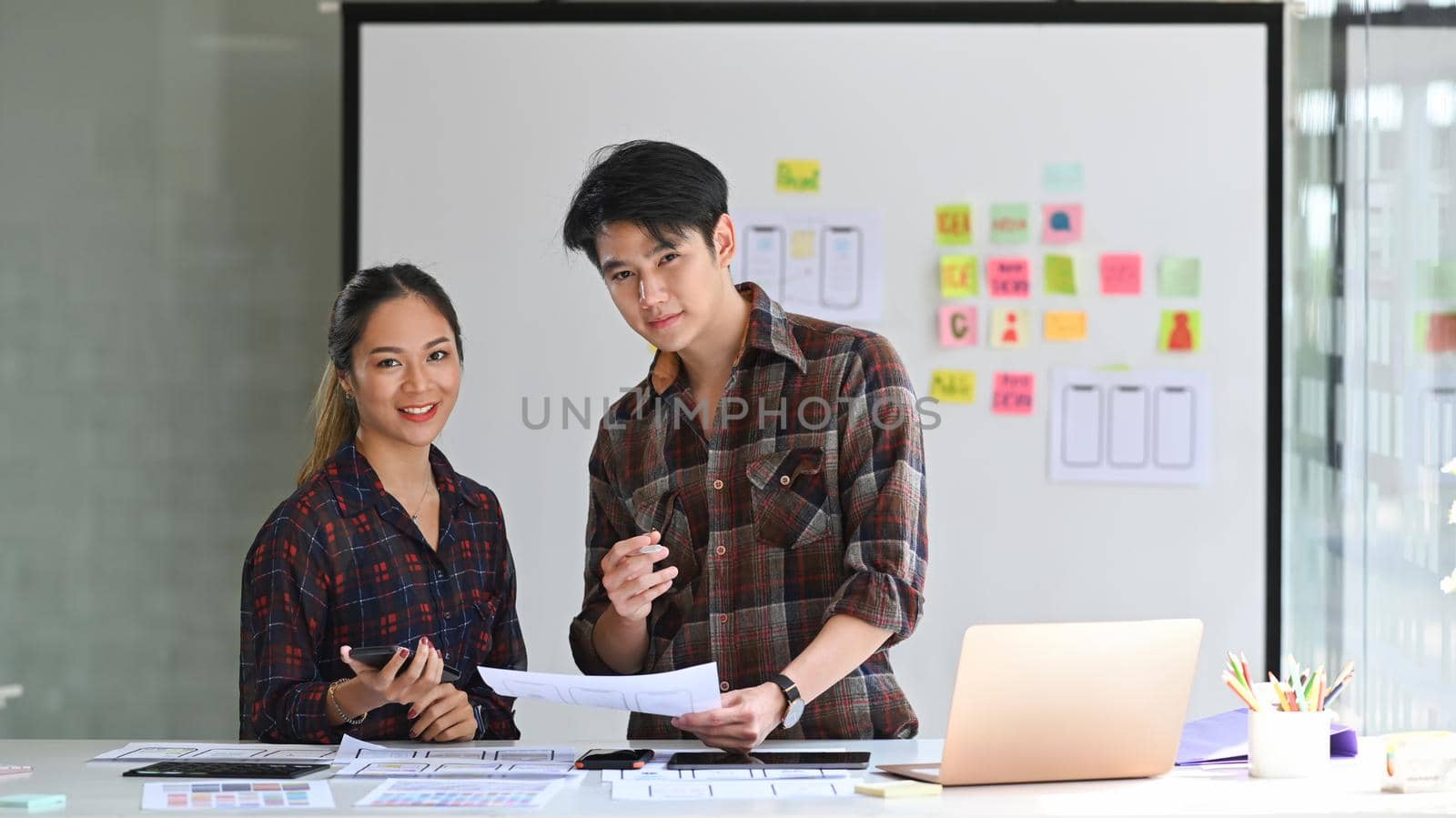 Two professionals web developers standing in bright modern office and smiling to camera.