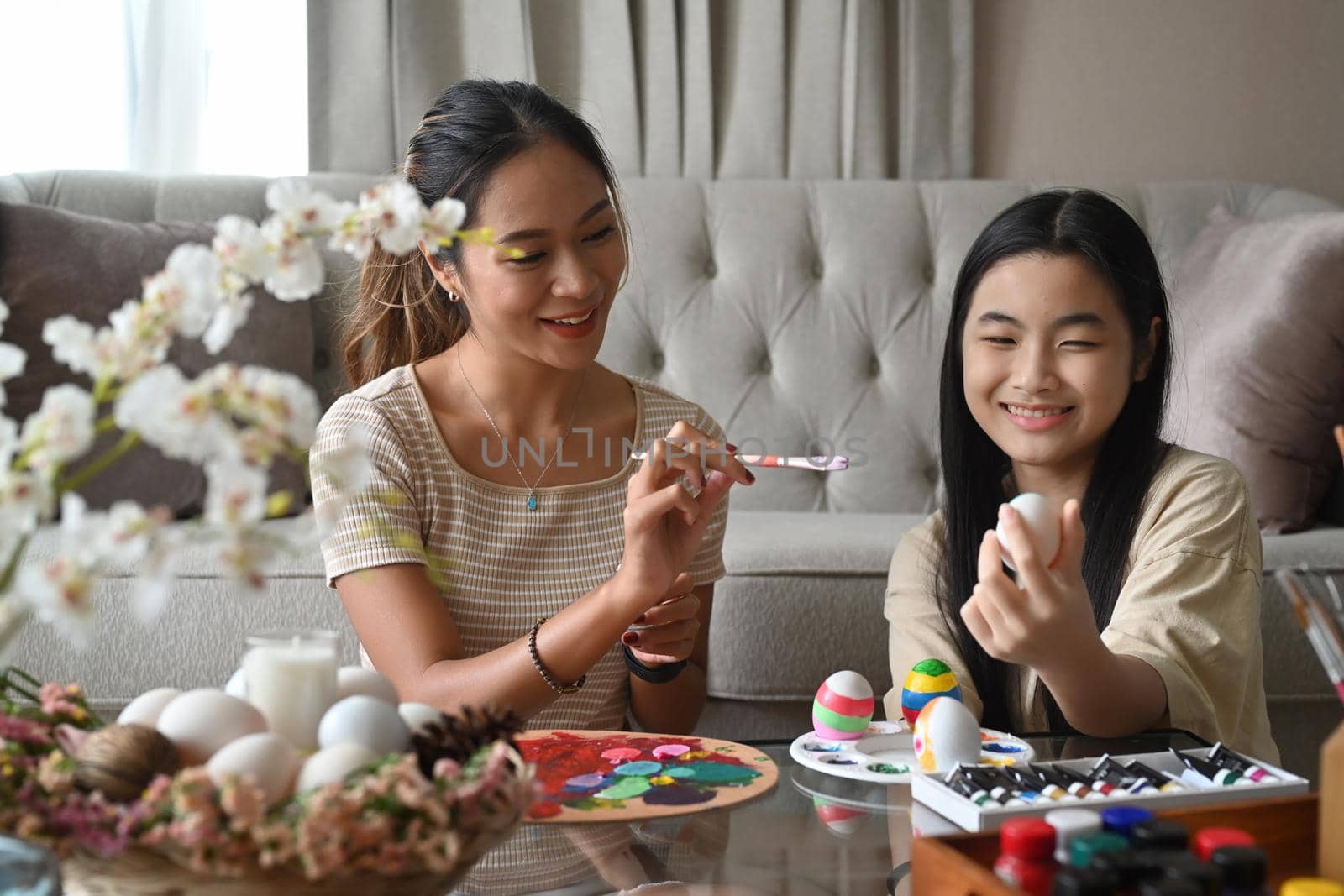Mother and daughter are spending leisure time together before Easter while painting eggs.
