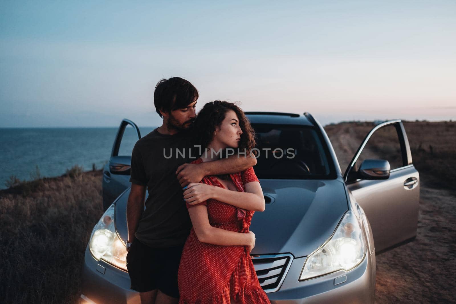 Young Couple Man and Woman Hugging Near Their SUV Car on Seaside After Sunset, Lovers Enjoying Moment Together