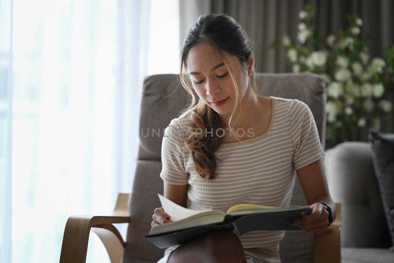 Peaceful millennial woman relaxing on armchair and reading book. by prathanchorruangsak