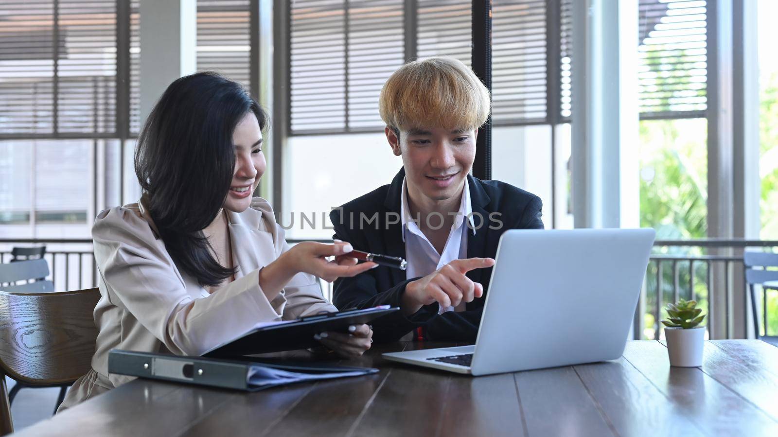 Two young businesspeople using computer laptop and discussing on new startup project together by prathanchorruangsak