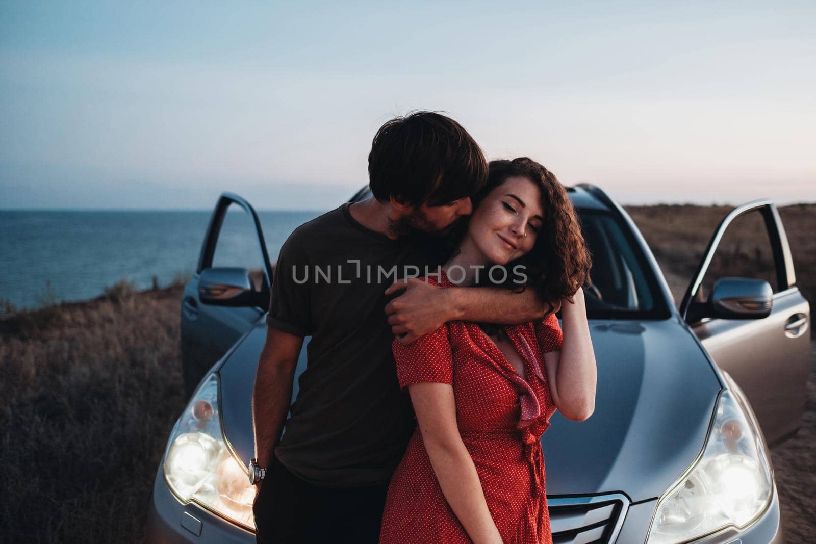 Young Couple Man and Woman Hugging and Kissing Near Their SUV Car on Seaside After Sunset, Lovers Enjoying Moment Together