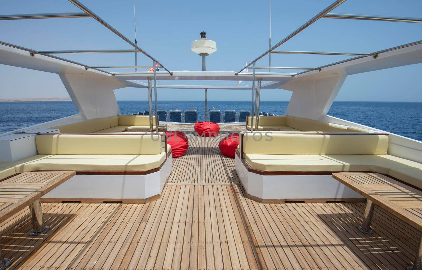 Teak wooden sundeck of a large luxury motor yacht with chairs sofa table and tropical sea view background