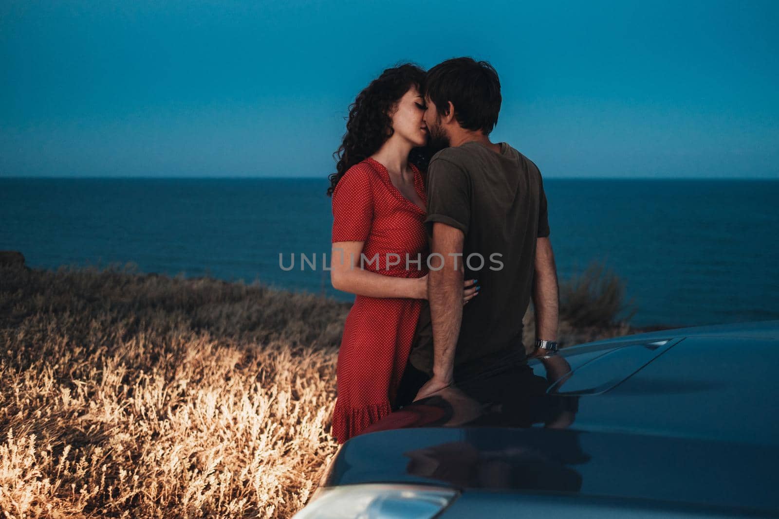 Young Couple Man and Woman Kissing and Hugging Near Their Car on Coastline at Nightfall