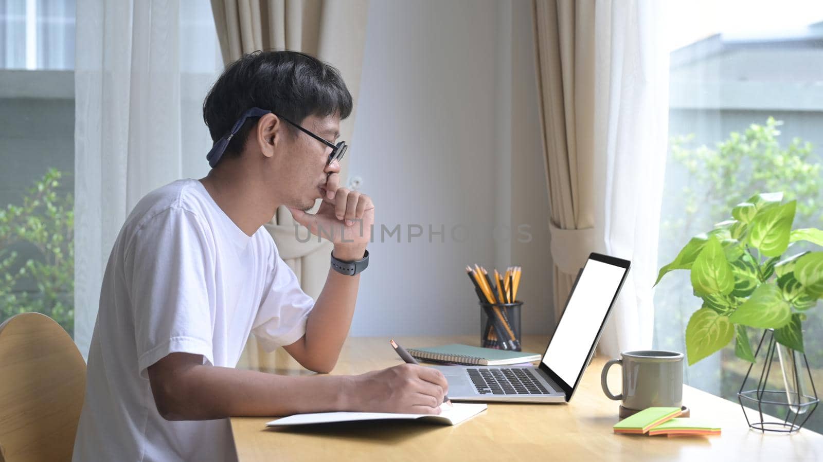 Focused asian man using laptop, reading email, working online at home office.