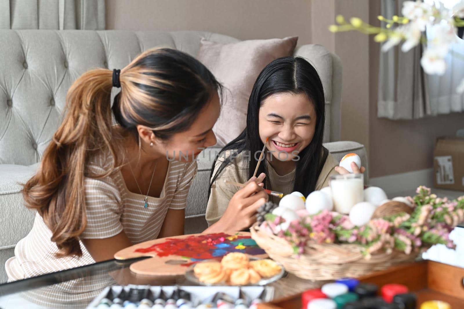 Mother drawing her daughter face while painting Easter eggs together.
