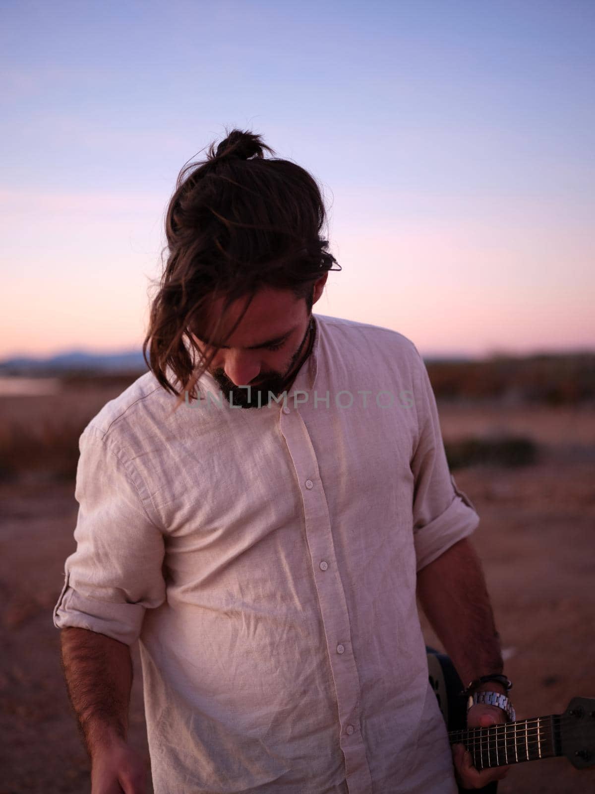 musician in a shirt facing the ground and with a guitar in his hand, vertical background in nature