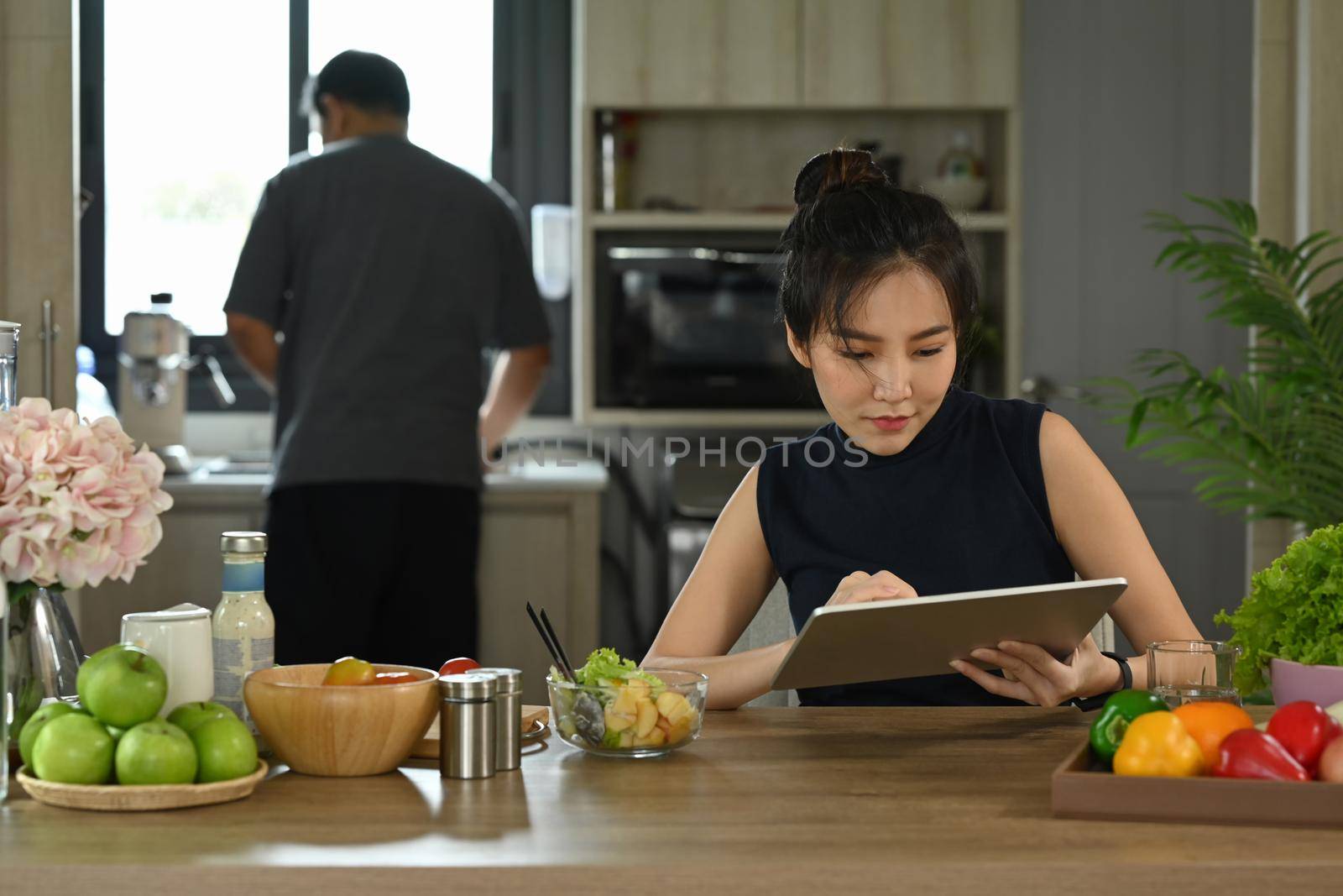 Asian housewife sitting in home and surfing internet on digital tablet.