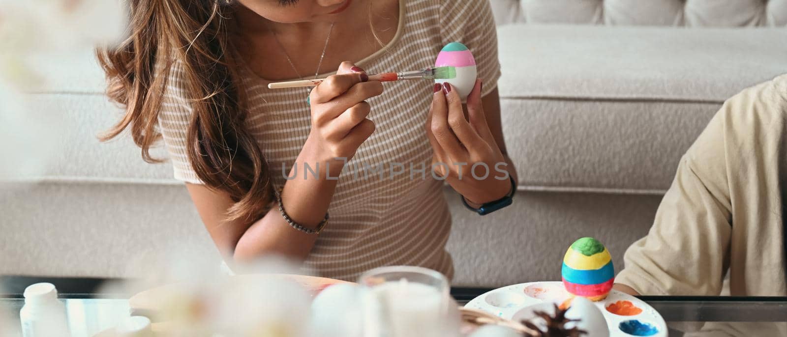 Young woman holding paintbrush and painting egg for Easter festivity. by prathanchorruangsak