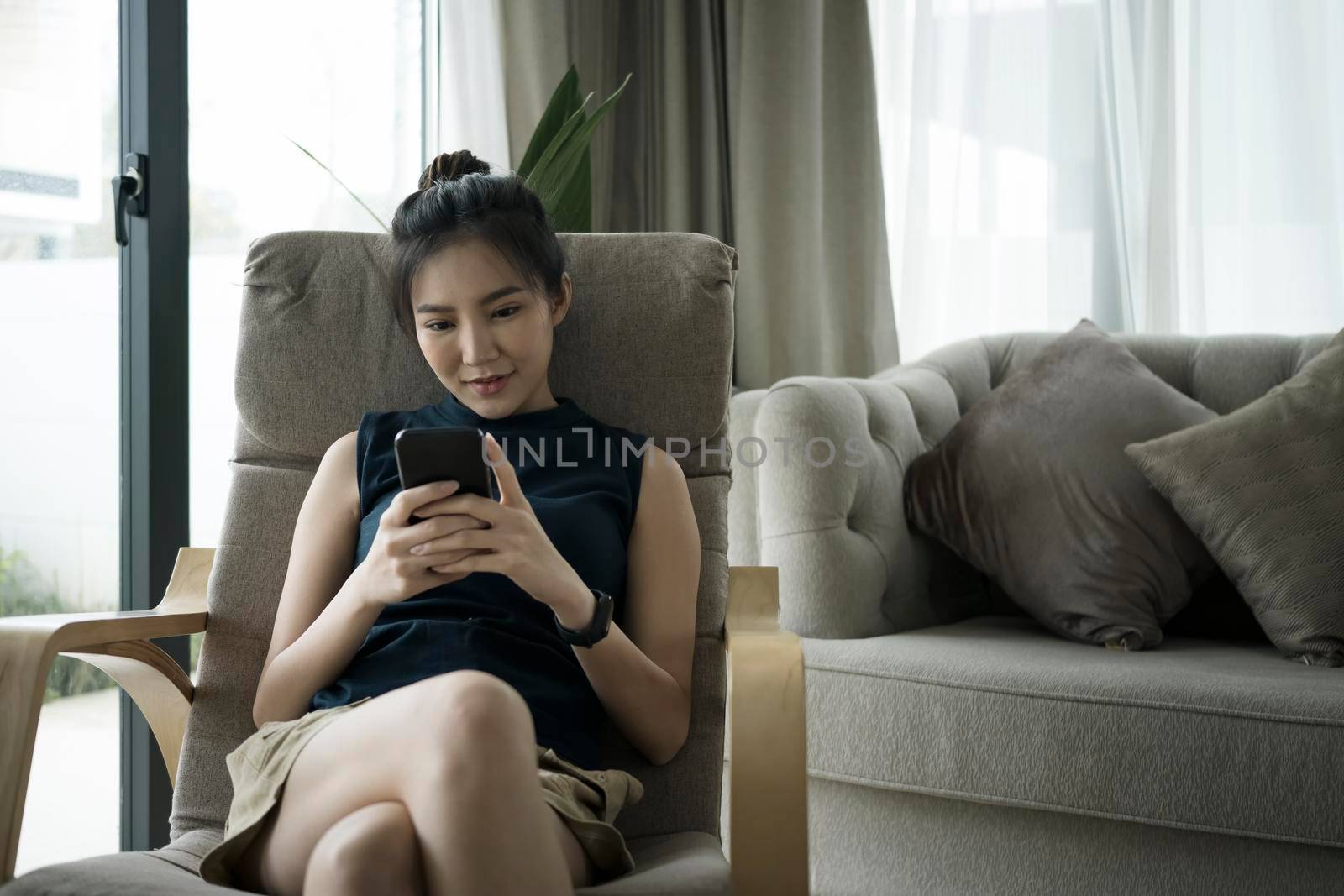 Millennial woman using smart phone while relaxing on armchair. by prathanchorruangsak