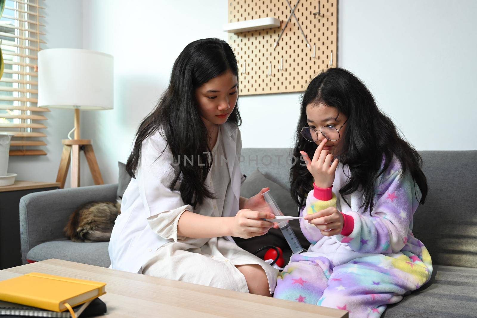 Cute asian girl medical uniform playing as doctor with her young sister at home.