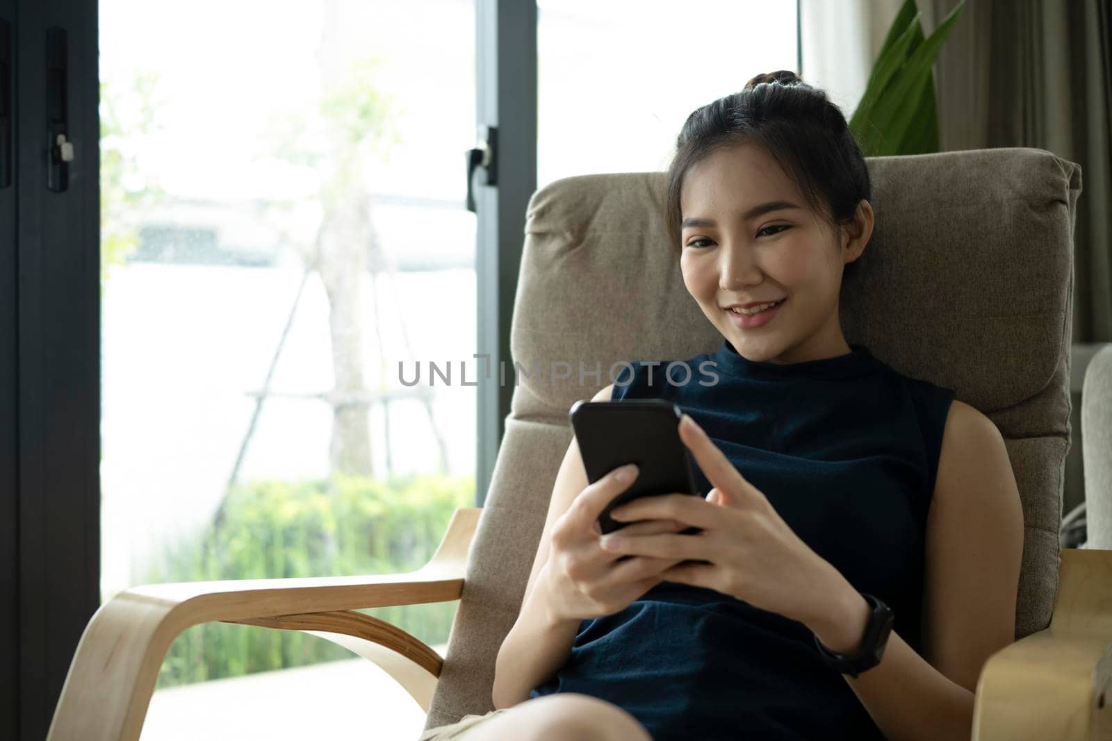 Pretty asian woman resting on armchair and using smart phone. by prathanchorruangsak