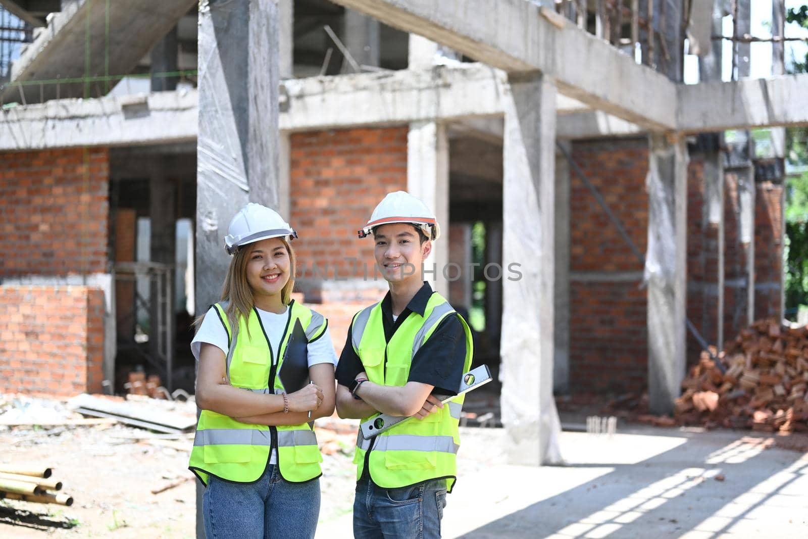 Two young engineer standing construction site and smiling to camera.